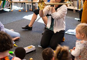 Éveil musical à la médiathèque Médiasud. Une personne joue d'un instrument de musique devant un public d'enfants et d'adultes. 